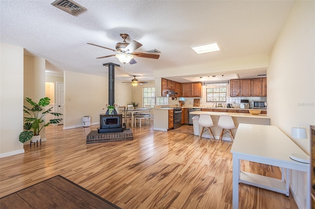 living area featuring a wood stove, light wood-style flooring, ceiling fan, a textured ceiling, and baseboards