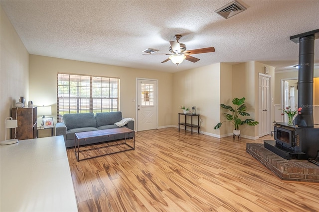 living area with a wood stove, light wood finished floors, ceiling fan, a textured ceiling, and baseboards
