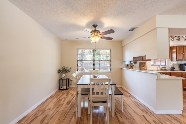dining room featuring light wood-type flooring, ceiling fan, a textured ceiling, and baseboards