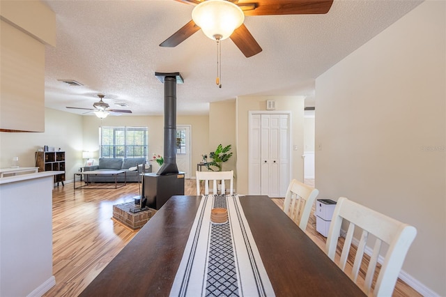 dining space featuring a wood stove, ceiling fan, light wood-style floors, a textured ceiling, and baseboards