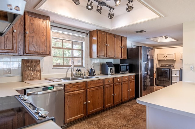 kitchen with a sink, stainless steel appliances, brown cabinetry, and a tray ceiling