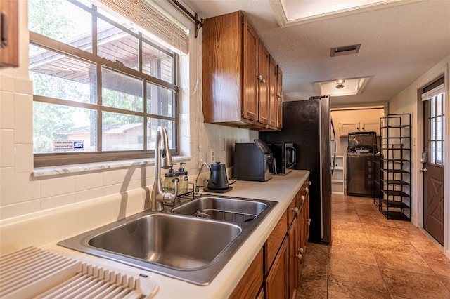 kitchen featuring brown cabinetry, a sink, light tile patterned flooring, a textured ceiling, and freestanding refrigerator