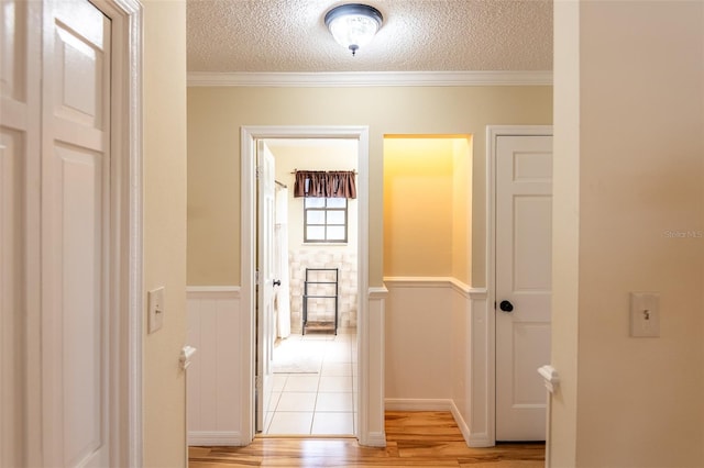 hallway featuring light wood-style flooring, a wainscoted wall, a textured ceiling, and ornamental molding