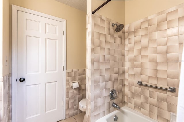 bathroom featuring tile walls, bathtub / shower combination, toilet, tile patterned floors, and a wainscoted wall