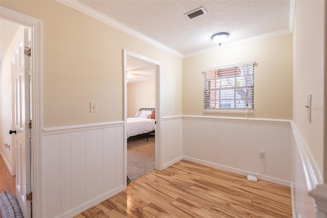 hall featuring wood finished floors, wainscoting, a textured ceiling, and ornamental molding