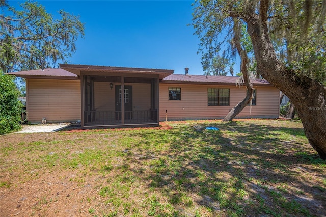 rear view of property with a sunroom, a yard, and metal roof
