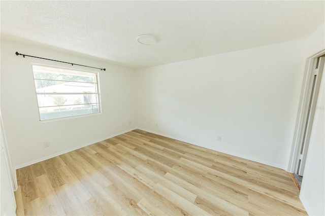 empty room with light wood-type flooring, a textured ceiling, and baseboards