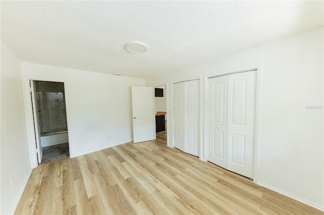 unfurnished bedroom featuring multiple closets, light wood-style flooring, a textured ceiling, ensuite bathroom, and baseboards