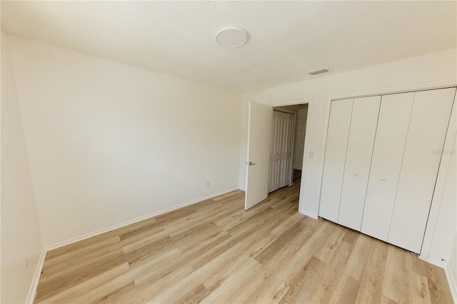 unfurnished bedroom featuring light wood-style floors, a closet, baseboards, and a textured ceiling