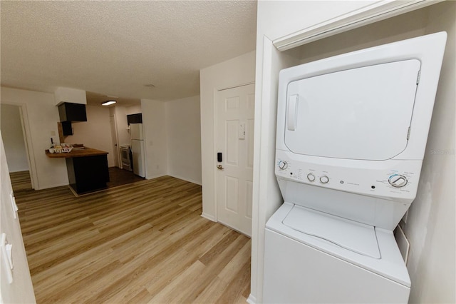 laundry area with estacked washer and dryer, light wood-style floors, a textured ceiling, and baseboards