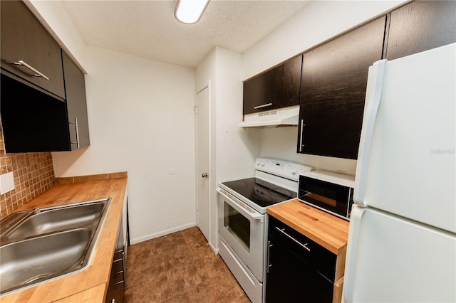 kitchen with white appliances, under cabinet range hood, wood counters, backsplash, and a sink