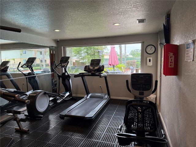 gym with a textured wall, a textured ceiling, healthy amount of natural light, recessed lighting, and baseboards
