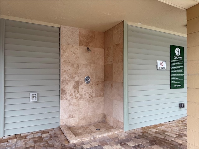 bathroom featuring a tile shower and brick patterned floors