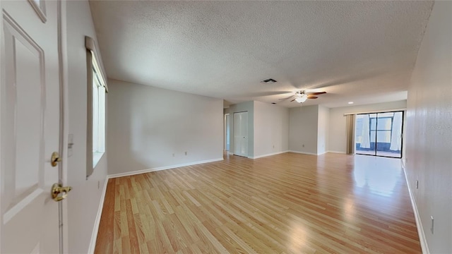 empty room with a textured ceiling, light wood-style floors, ceiling fan, and baseboards