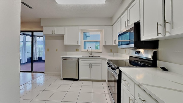 kitchen with appliances with stainless steel finishes, a sink, light countertops, white cabinetry, and a textured ceiling