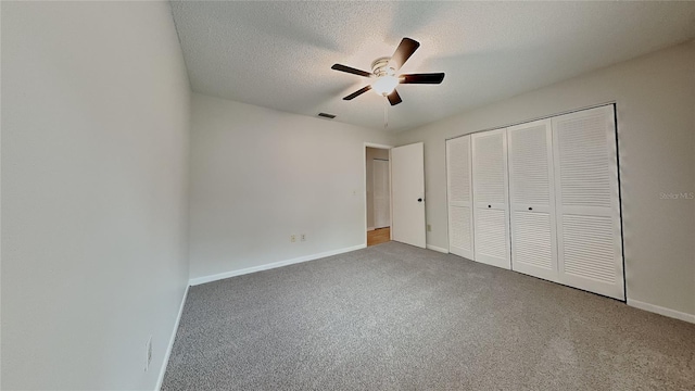 unfurnished bedroom with carpet flooring, a closet, baseboards, a textured ceiling, and a ceiling fan