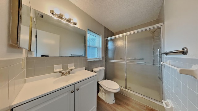 bathroom featuring tile walls, a shower stall, a textured ceiling, toilet, and vanity