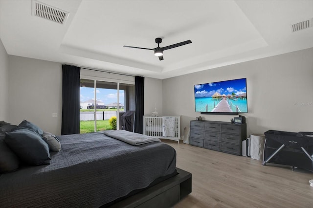 bedroom with a raised ceiling, access to outside, wood finished floors, and a ceiling fan