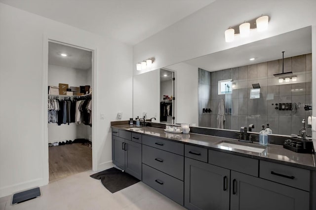 bathroom featuring walk in shower, double vanity, a walk in closet, baseboards, and tile patterned floors