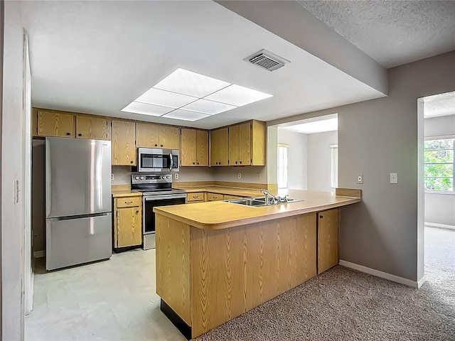 kitchen with stainless steel appliances, light countertops, a peninsula, a sink, and baseboards