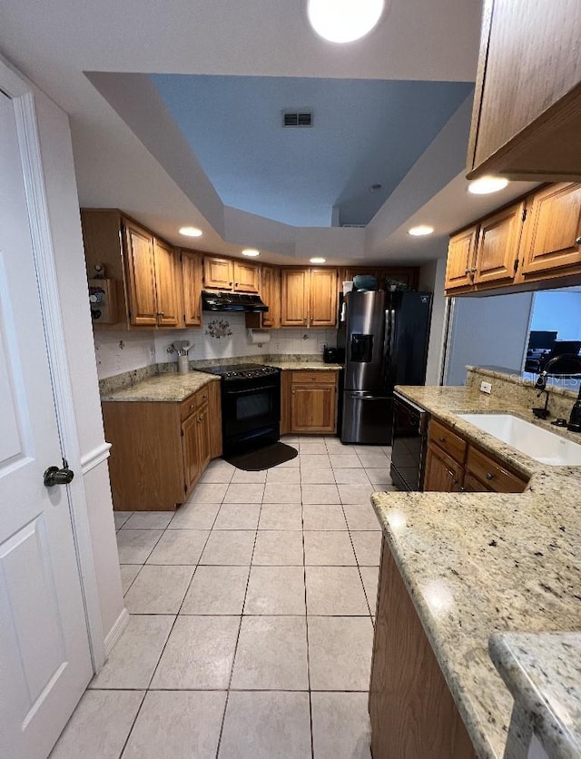 2528 Deerbrook Dr, Lakeland, FL 33811 - kitchen with black appliances, a tray ceiling, a sink, brown cabinets, and light stone countertops