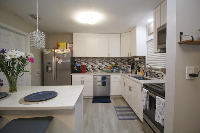 kitchen featuring stainless steel appliances, a sink, backsplash, light wood-style floors, and white cabinetry