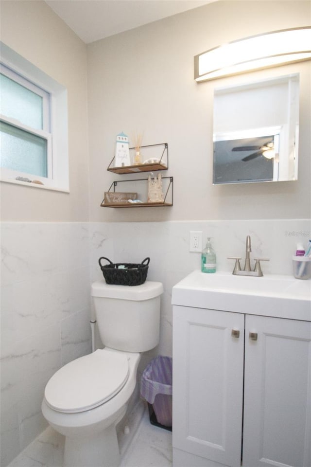 bathroom with marble finish flooring, tile walls, vanity, toilet, and wainscoting