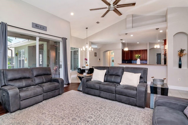 living room featuring a chandelier, ceiling fan, vaulted ceiling, baseboards, and arched walkways