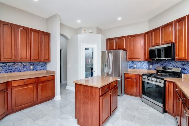 kitchen featuring appliances with stainless steel finishes, arched walkways, backsplash, a center island, and light stone countertops