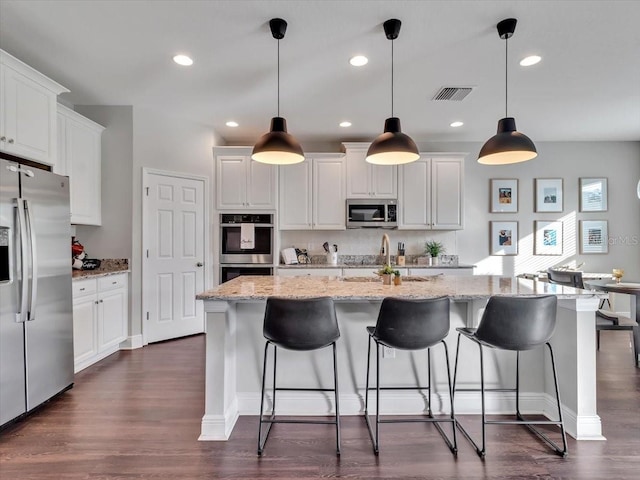 kitchen with appliances with stainless steel finishes, dark wood-style flooring, white cabinetry, a center island with sink, and recessed lighting