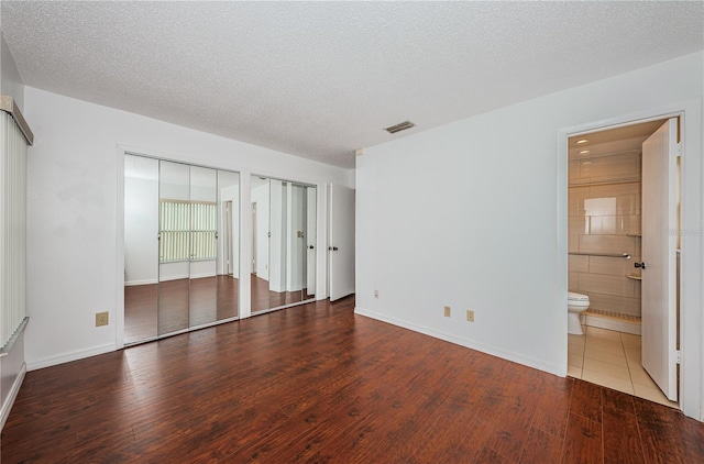 10051 82nd Ln, Seminole, FL 33777 - unfurnished bedroom with wood finished floors, two closets, a textured ceiling, baseboards, and ensuite bath