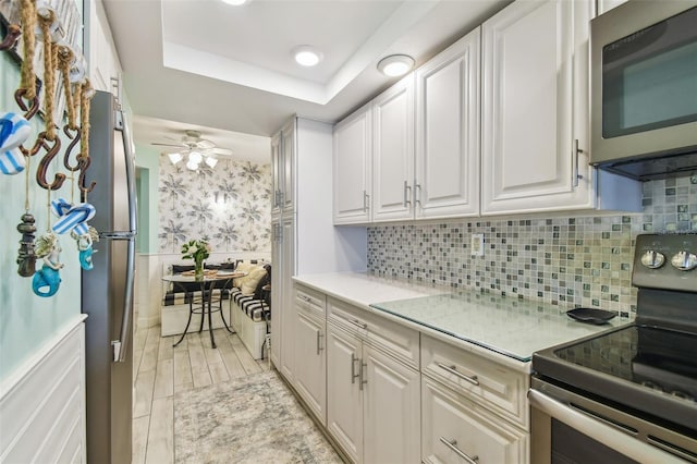 17980 Gulf Blvd Unit 505, Redington Shores, FL 33708 - kitchen with stainless steel appliances, white cabinets, a raised ceiling, ceiling fan, and tasteful backsplash