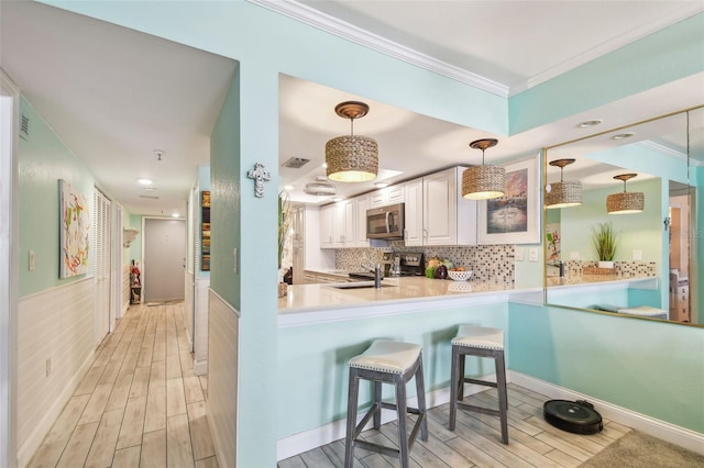 17980 Gulf Blvd Unit 505, Redington Shores, FL 33708 - kitchen featuring stainless steel appliances, crown molding, light wood finished floors, a kitchen bar, and hanging light fixtures