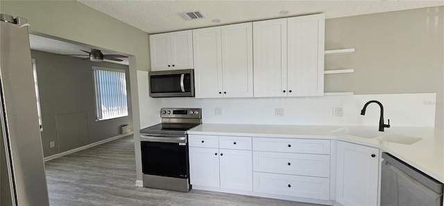 kitchen featuring appliances with stainless steel finishes, open shelves, a sink, white cabinets, and light wood-style flooring