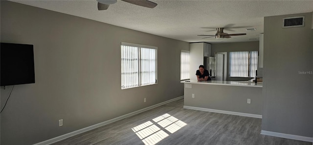 unfurnished living room featuring a ceiling fan, wood finished floors, a textured ceiling, and baseboards
