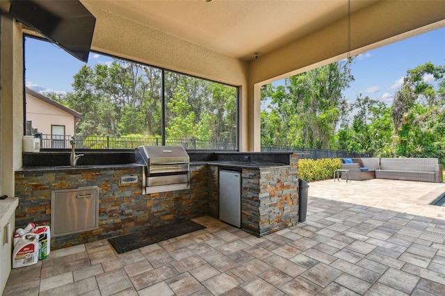view of patio featuring a grill, exterior kitchen, a fenced backyard, view of wooded area, and a sink