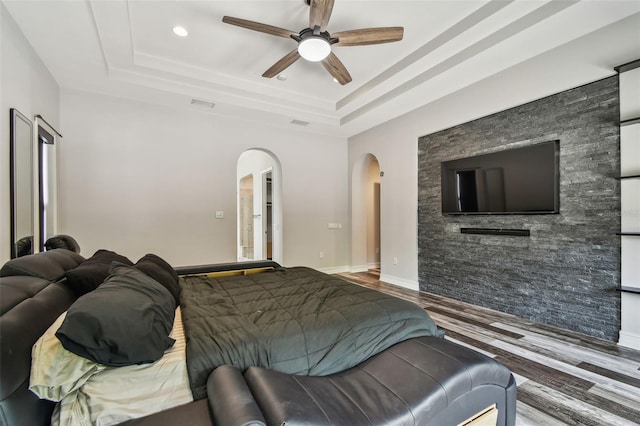 bedroom with arched walkways, a raised ceiling, wood finished floors, a ceiling fan, and baseboards