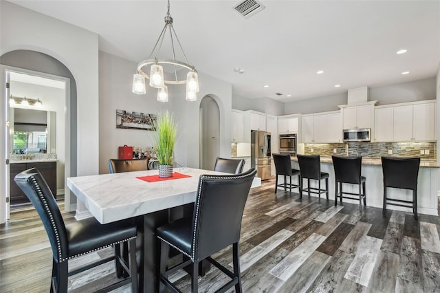 dining space featuring dark wood-type flooring, a chandelier, arched walkways, and recessed lighting