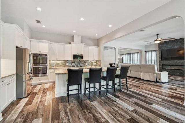 kitchen featuring stainless steel appliances, dark wood finished floors, open floor plan, white cabinetry, and backsplash