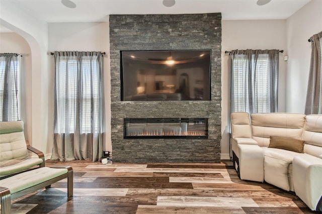 living room with wood finished floors, a stone fireplace, arched walkways, and plenty of natural light