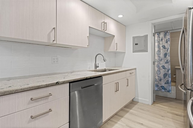 kitchen with stainless steel appliances, a sink, electric panel, light wood finished floors, and light stone countertops