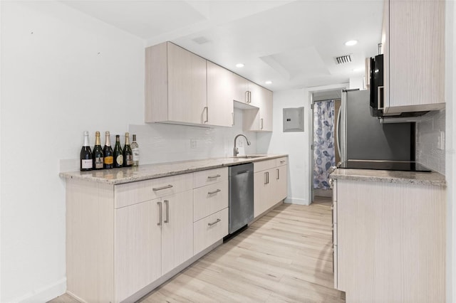 kitchen featuring stainless steel appliances, a sink, light wood finished floors, backsplash, and baseboards