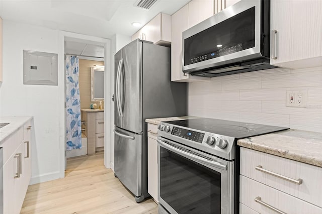 kitchen featuring stainless steel appliances, electric panel, light wood-style floors, light stone countertops, and backsplash