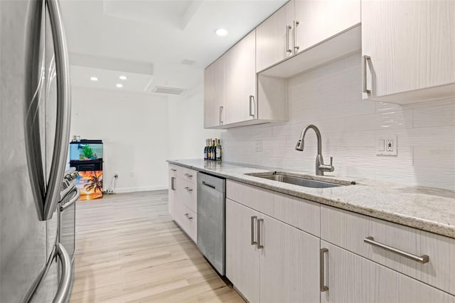 kitchen with appliances with stainless steel finishes, a sink, light wood-style floors, backsplash, and light stone countertops