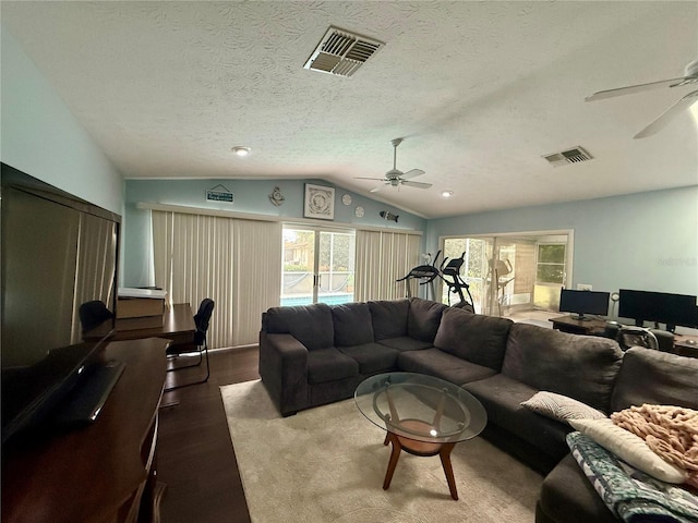 living area with ceiling fan, lofted ceiling, wood finished floors, healthy amount of natural light, and a textured ceiling