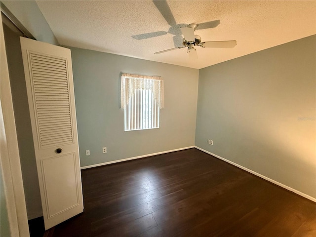 unfurnished bedroom with dark wood-style floors, a textured ceiling, baseboards, and ceiling fan