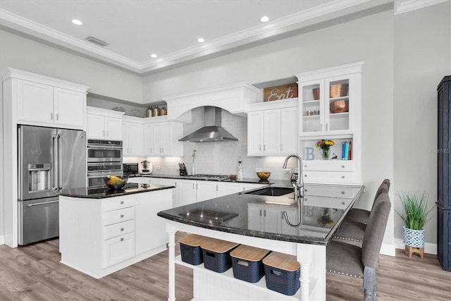 kitchen featuring stainless steel appliances, wall chimney range hood, a sink, a center island, and light wood finished floors