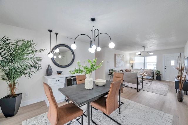 dining area featuring a chandelier, light wood-style floors, baseboards, and wine cooler
