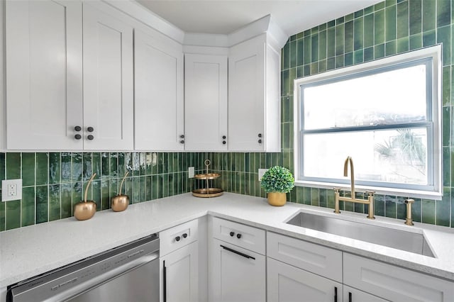 kitchen featuring stainless steel dishwasher, a sink, white cabinetry, and tasteful backsplash