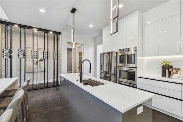 kitchen with appliances with stainless steel finishes, a sink, modern cabinets, white cabinetry, and a center island with sink